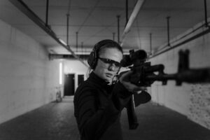Focused woman aiming with a rifle at an indoor shooting range in black and white.